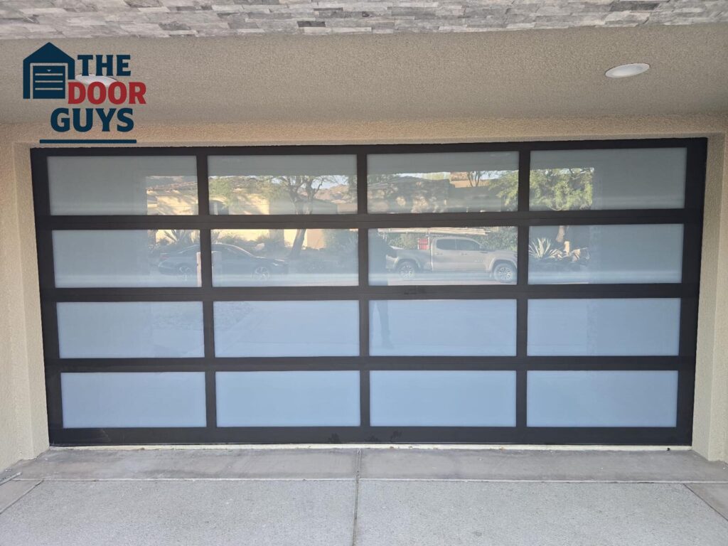 Custom glass garage door with black frame, modern style, and full-view panels, installed by The Door Guys garage door experts.
