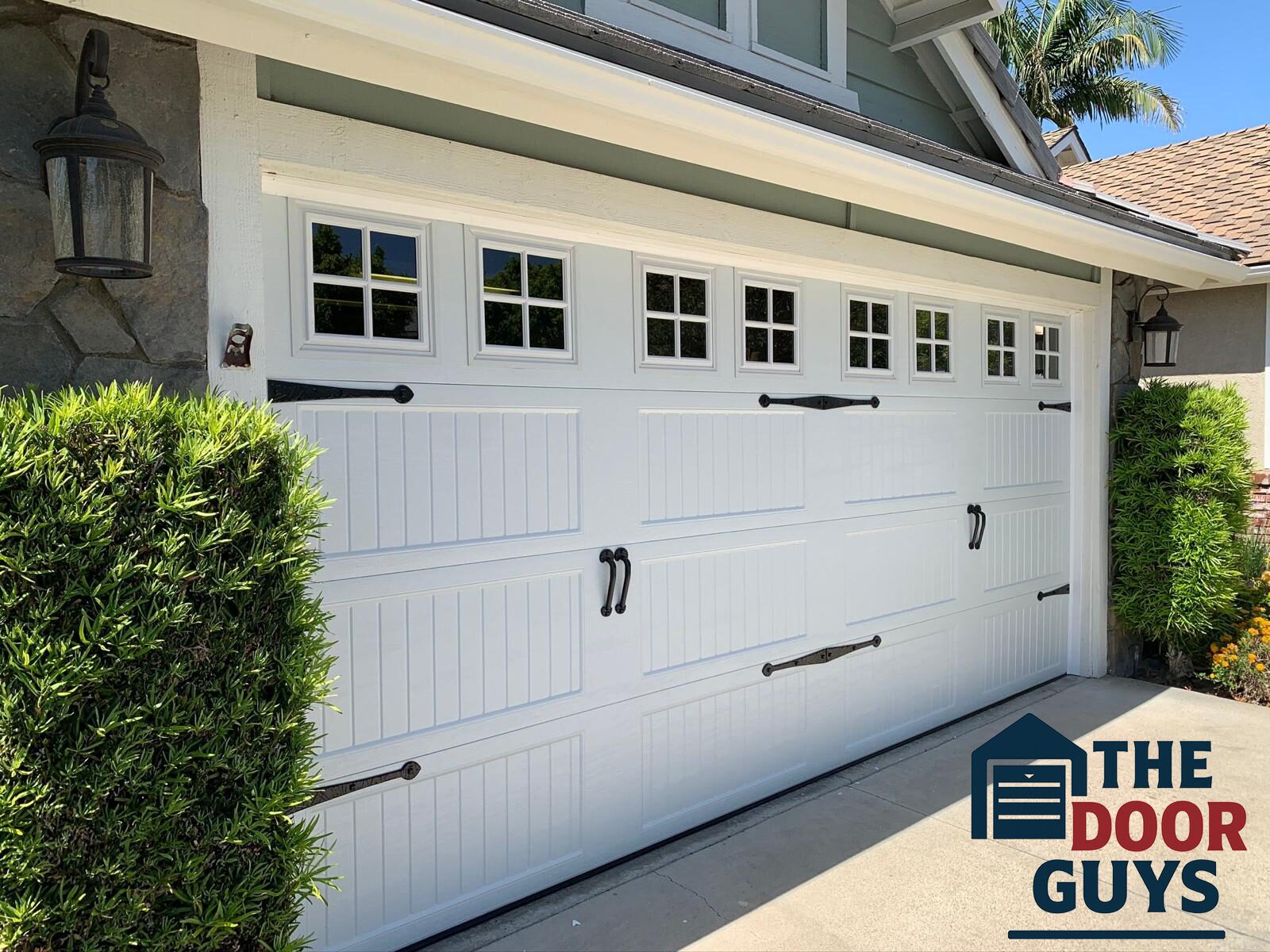 New carriage-style garage door with upper windows and black decorative handles, installed by The Door Guys.